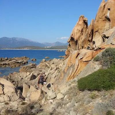 a man walking on rocks near a body of water at Appartement T2bis Sartène 60m2 avec jolie terrasse de 25m2 et vue panoramique mer et montagne sur le Golfe du Valinco - Quartier calme à 10mn à pied du centre ville - Idéal pour 4 personnes et possibilité de 6 couchages - Place de parking réservée in Sartène