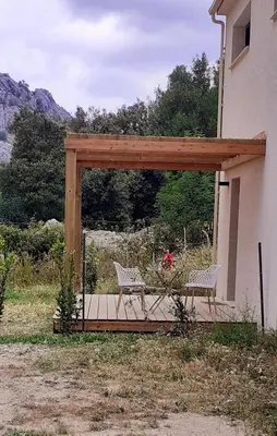 two chairs and a table under a wooden pergola at Casa Prunelli 2 in Omessa
