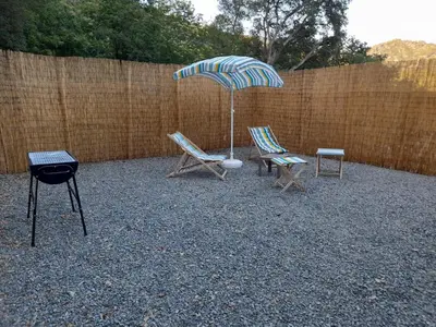 a patio with two chairs and an umbrella and a grill at Maisonnette U Santu Ghjuvandria ou A Santa Ghjulia entre mer et Montagne in Volpajola