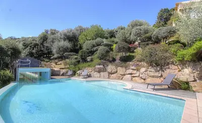a large swimming pool with a chair next to a mountain at Appartement vue mer en Résidence avec piscine in Porto-Vecchio