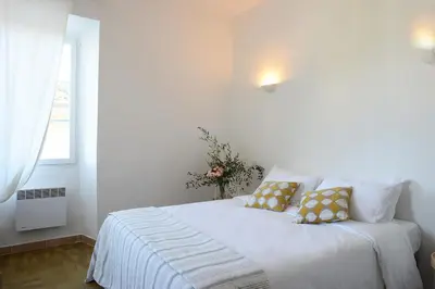 a white bedroom with a white bed with yellow pillows at Au coeur du Village de Lucciana in Lucciana