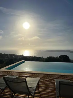 a swimming pool with two chairs and the sun in the sky at Appartement 4A villa cargese in Cargèse