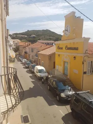 a street with cars parked in front of a building with a clock at Charmant 2 pièces en plein coeur du village in Cargèse