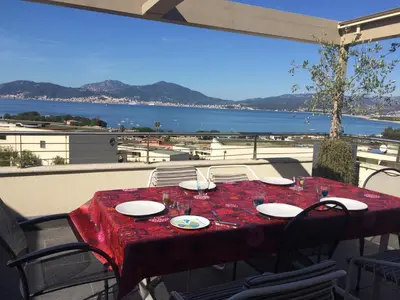 a table with a red tablecloth on a balcony with a view of the water at VUE MAGNIFIQUE SUR BAIE AJACCIO in Porticcio