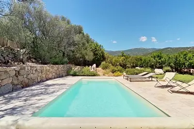 a swimming pool with two chairs and a stone wall at Bergeries de l'Argiale - ARGHJALE - hôtel in Figari