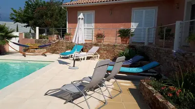 a patio with chairs and a hammock next to a pool at Villa BRIMI in Ghisonaccia