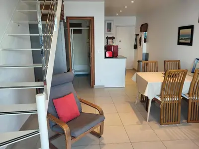a living room with a staircase and a chair with a red pillow at Un balcon sur la mer - Duplex 60 m2 - Chambres à l'étage - Pieds dans l'eau - Accès plage sans route à traverser in Porticcio