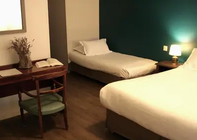 a hotel room with two beds and a desk and a table at Hôtel Albion in Ajaccio