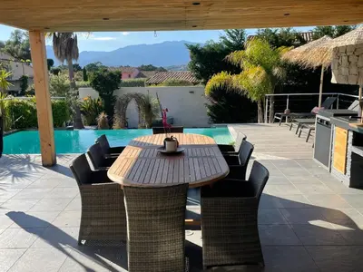 a wooden table and chairs next to a swimming pool at Villa CASA BAGGIA, proche plage, piscine à débordement chauffée, pool house in Porto-Vecchio