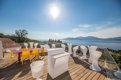 a deck with a table and chairs and a view of the water at Domain U Tempu Persu Sleeps 12 with Park in Porticcio