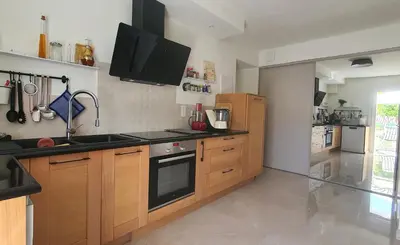 a kitchen with wooden cabinets and a tv on the wall at Charmant appartement en Rez de jardin in Sartène
