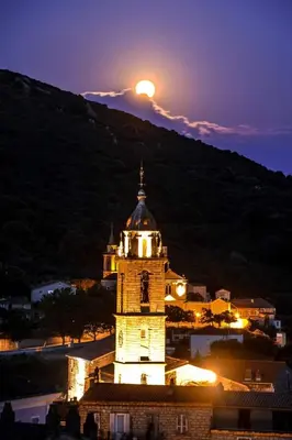 a clock tower at night with the moon in the sky at Charmant appartement en Rez de jardin in Sartène
