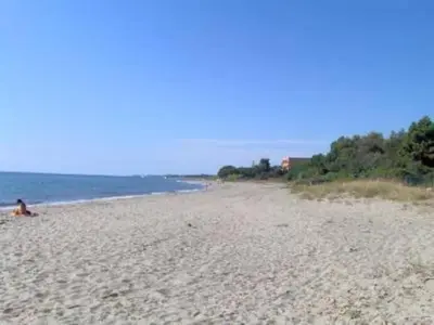 a person sitting on a sandy beach next to the ocean at Appartement T2 Bord de Mer - Maria Beach in Santa-Lucia-di-Moriani