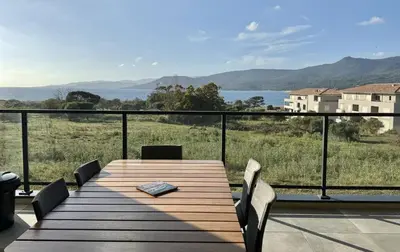 a wooden table on a balcony with a view of the water at BEL'ORIZONTE Proche centre ville et plage, vue mer in Propriano