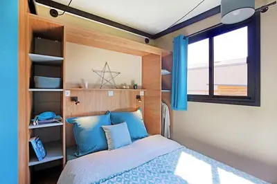 a bedroom with a bed with blue pillows and a window at Camping l'Oso in Porto-Vecchio