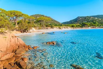 a beach with clear blue water and rocks at Camping l'Oso in Porto-Vecchio