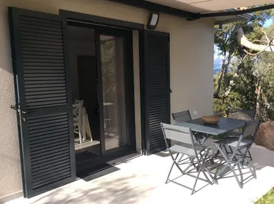 a patio with black doors and a table and chairs at Coquet appartement indépendant entre mer et maquis in Sotta
