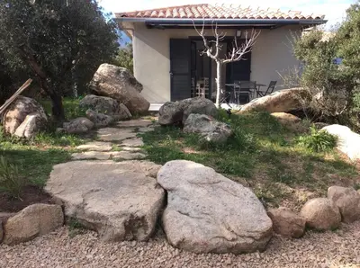a garden with rocks and a house in the background at Coquet appartement indépendant entre mer et maquis in Sotta