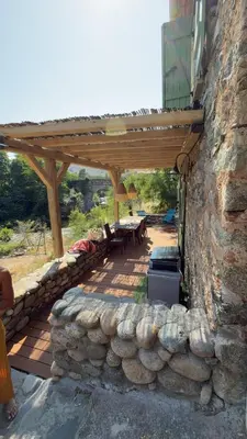 a patio with a stone wall and a wooden pergola at A Casetta d’Hélène et Jeanette in Omessa