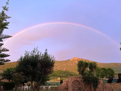a rainbow in the sky with chairs and trees at Maison Le Prunier avec piscine - Domaine E Case Di Cuttoli in Cuttoli-Corticchiato