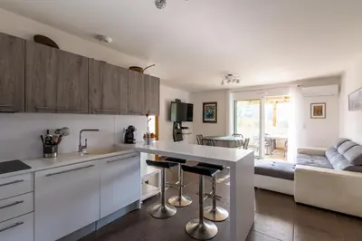 a kitchen with white cabinets and a living room at Le Clos d'Oletta in Oletta