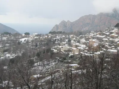 a small town on a snowy hill with houses at Hôtel Aïtone in Evisa