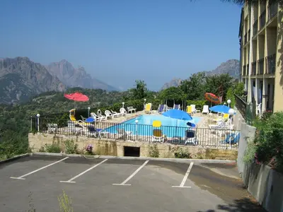 a pool with chairs and umbrellas in a parking lot at Hôtel Aïtone in Evisa