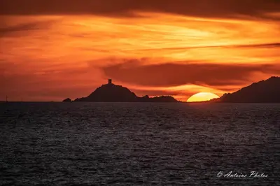 a sunset with a lighthouse on an island in the ocean at Cosystudio centre Ajaccio in Ajaccio