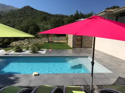 a red umbrella sitting next to a swimming pool at Villa Récente avec Piscine proche L'ILE ROUSSE in Ville-di-Paraso