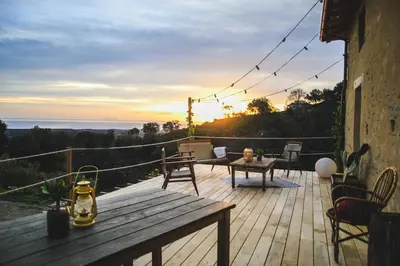 a wooden deck with a table and chairs and the sunset at Eco Gîte avec vue sur mer in Chiatra