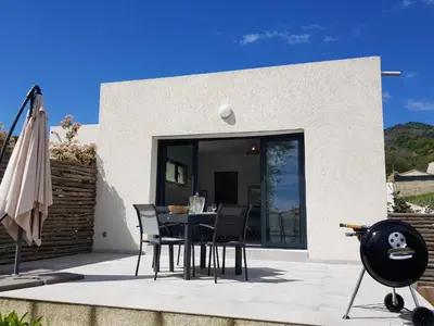 a patio with a table and chairs and an umbrella at Maisons T2 avec jardins privatifs - 10mn de la plage et 5mn du village - Casa di i trinelli in Vescovato