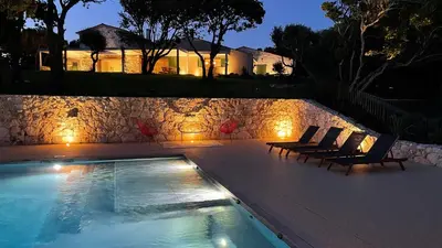 a swimming pool with two chairs next to a stone wall at Villa Arbevhio in Bonifacio
