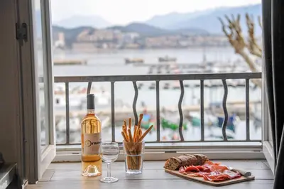 a bottle of wine and a plate of food next to a window at Les Studios du Pêcheur - Hypercentre - Clim - City Trip in Ajaccio