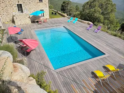 a swimming pool with chairs and umbrellas on a wooden deck at A Vignarella in Ventiseri