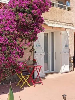 a red table and bench under a tree with pink flowers at Un Nid Douillet en bord de plage !! in Lucciana