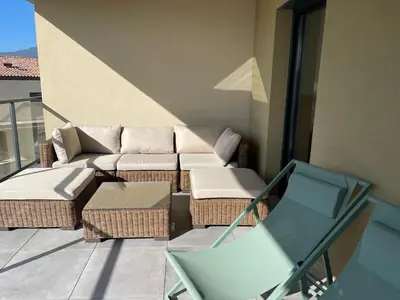 a patio with a couch and a chair on a balcony at Superbe T3 NEUF VUE MER in Propriano