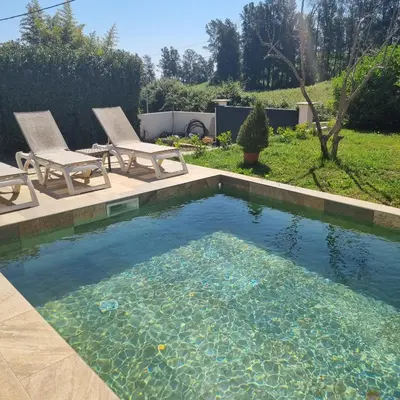 a swimming pool with two chairs and a pool of water at Rez de villa avec piscine privée, wifi, jardin clôturé in Penta-di-Casinca