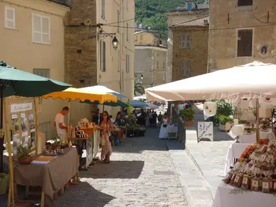 a group of people walking through a market with tables and umbrellas at Appartement A Caserella entièrement rénové avec terrasse et vue panoramique sur mer in Valle-di-Campoloro
