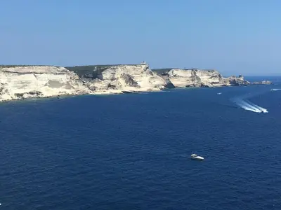 a boat in a large body of water with cliffs at Superbe appartement sur le port, jacuzzi, piscine in Porto-Vecchio