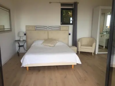 a bedroom with a large bed and a chair at Villa l'Alpana en bois vue mer a 180 degres in Sari Solenzara