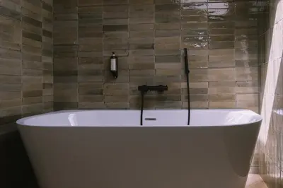 a white bath tub in a bathroom with a tile wall at L'Orangeraie d'Afa in Afa