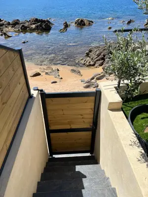 a set of stairs leading to a beach with a wooden door at PIEDS DANS L'EAU, TIUCCIA, appartement 2-4 pers in Casaglione