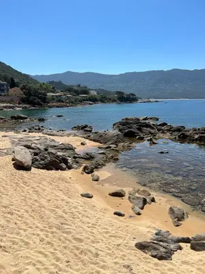 a sandy beach with rocks and water and mountains at PIEDS DANS L'EAU, TIUCCIA, appartement 2-4 pers in Casaglione