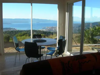 a table and chairs in a room with a view of the water at Gîtes Sassone, piscine, jacuzzi et vue mer panoramique sur Ajaccio in Alata