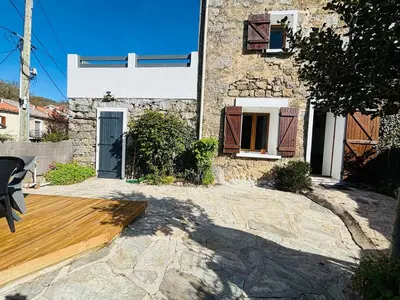 a stone house with a wooden deck in front of it at Belle maison de montagne proche Ajaccio in Bastelica