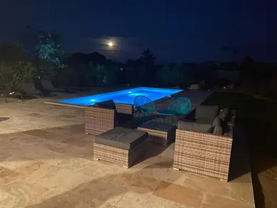 a swimming pool at night with wicker chairs and a table at Villa Chez Géraldine Piscine chauffée, proche plage et rivière in Lecci