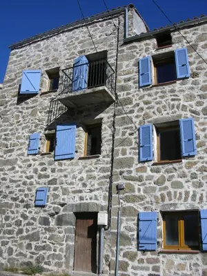 a stone building with blue shutters and a balcony at Maison Le Rêve in Evisa