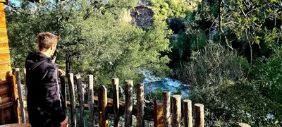 a man standing behind a fence looking at a river at GITES O FIL DE L'EAU piscine spa accès rivière in Omessa