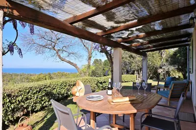 a table on a patio with a view of the ocean at Domaine Punta della Guardia villa vue mer dans nature protégée, plage à 1,5 km in Cervione