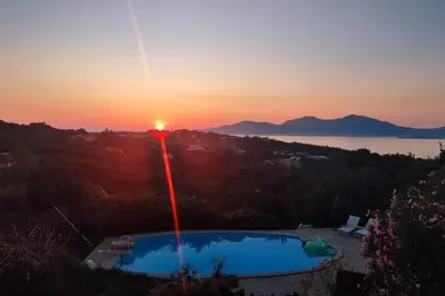 a sun setting over a swimming pool with the sunset in the background at F4 à Porticcio avec piscine et vue sur mer in Porticcio